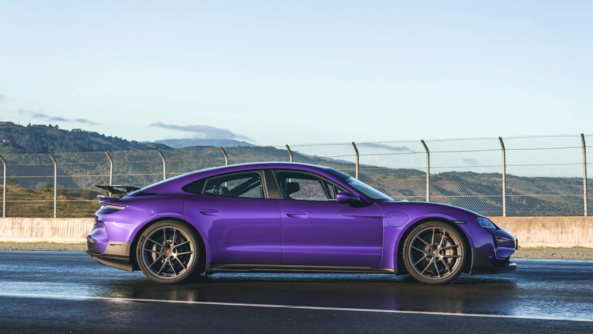 side view of the porsche taycan turbo gt parked on a race track with green hills behind