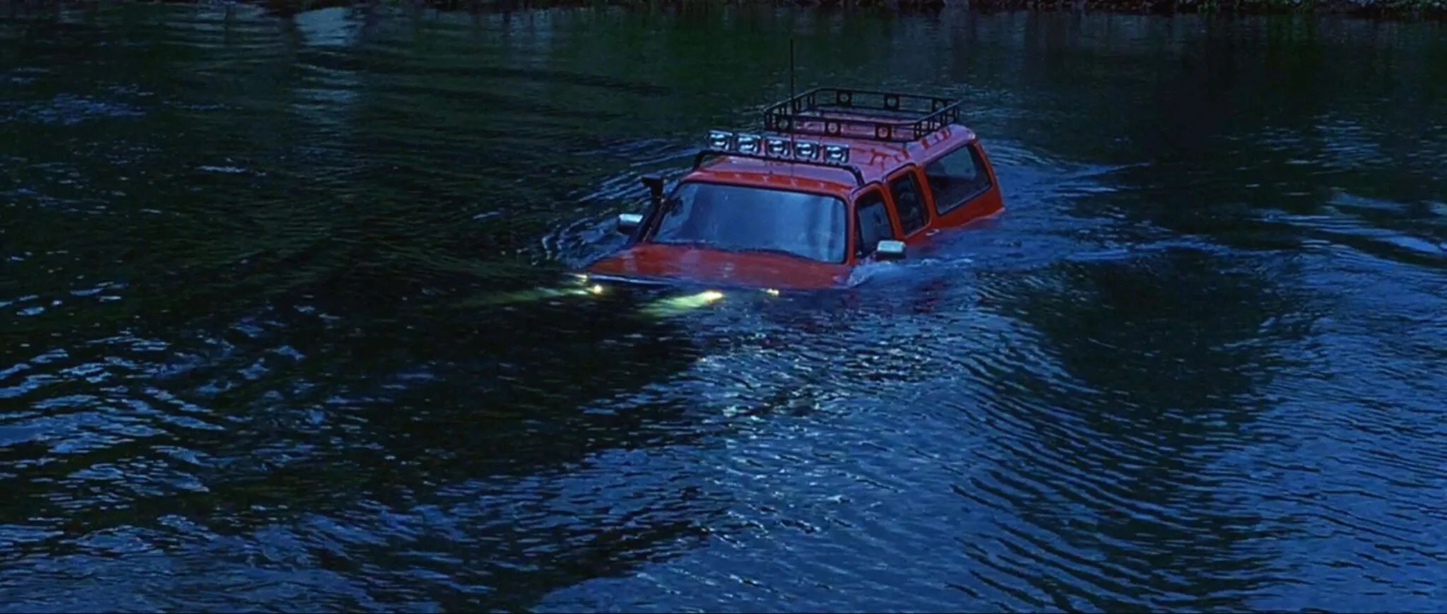 Image from 1997 movie Dante's Peak showing a red suburban driving through a river. 