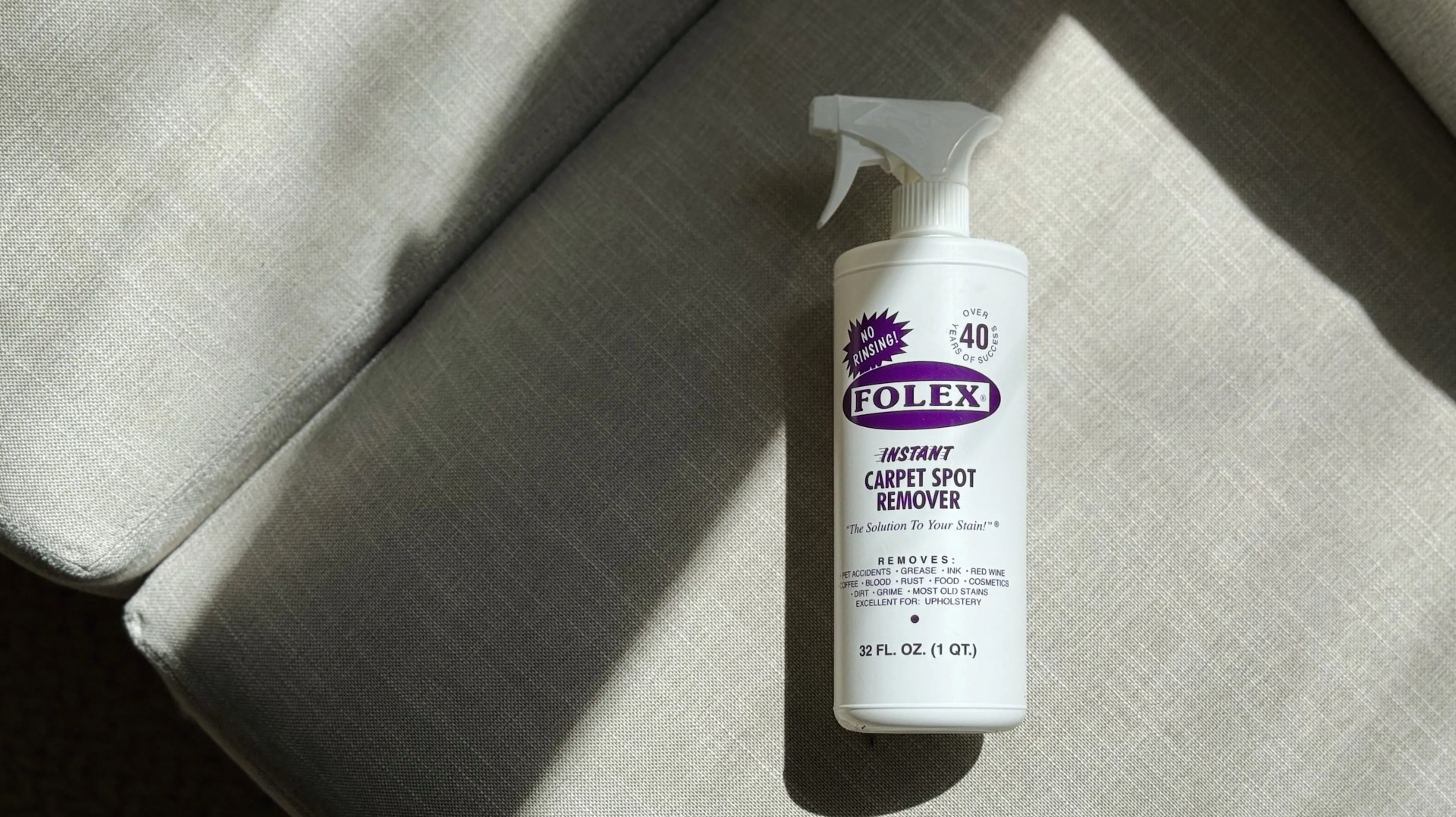 Bottle of Folex cleaner lying flat on white couch partially covered in shadow