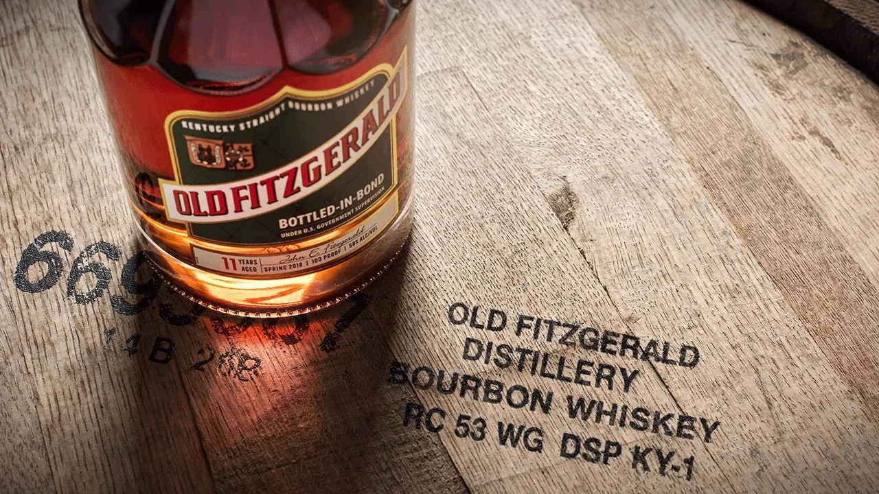 Old Fitzgerald bottled in bond bourbon shown from top down sitting on a whiskey barrel labeled old fitzgerald distillery.