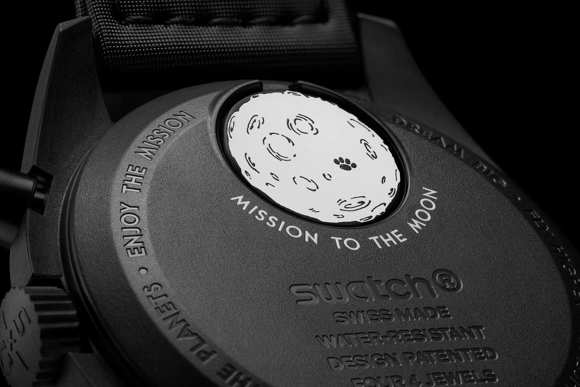 Close up photo of the Omega x Swatch Mission to Moonphase - New Moon caseback showing a white illustration of a cartoon moon with a Snoopy Paw print on the circular battery cover.