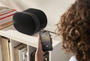 Person using the Sonos S2 app on iPhone to control an Era 300 speaker sitting on a nearby bookshelf
