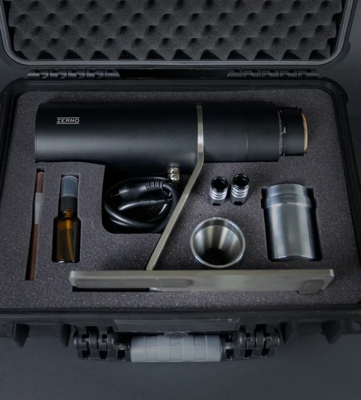 Zerno Z1 coffee grinder laying flat inside a hard-sided case with flat cutouts alongside its various parts. 
