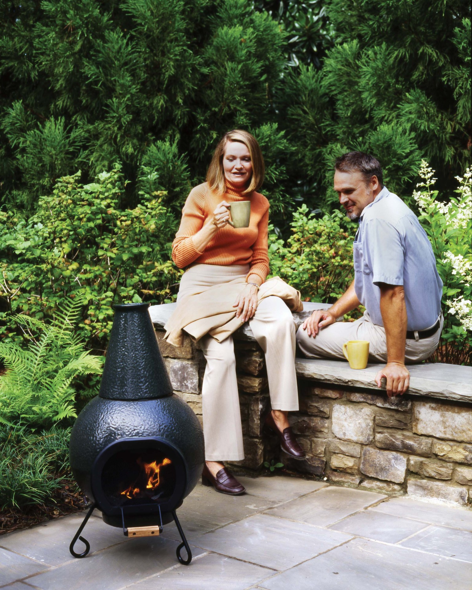 vintage photo of two people seated around a green outdoor fireplace
