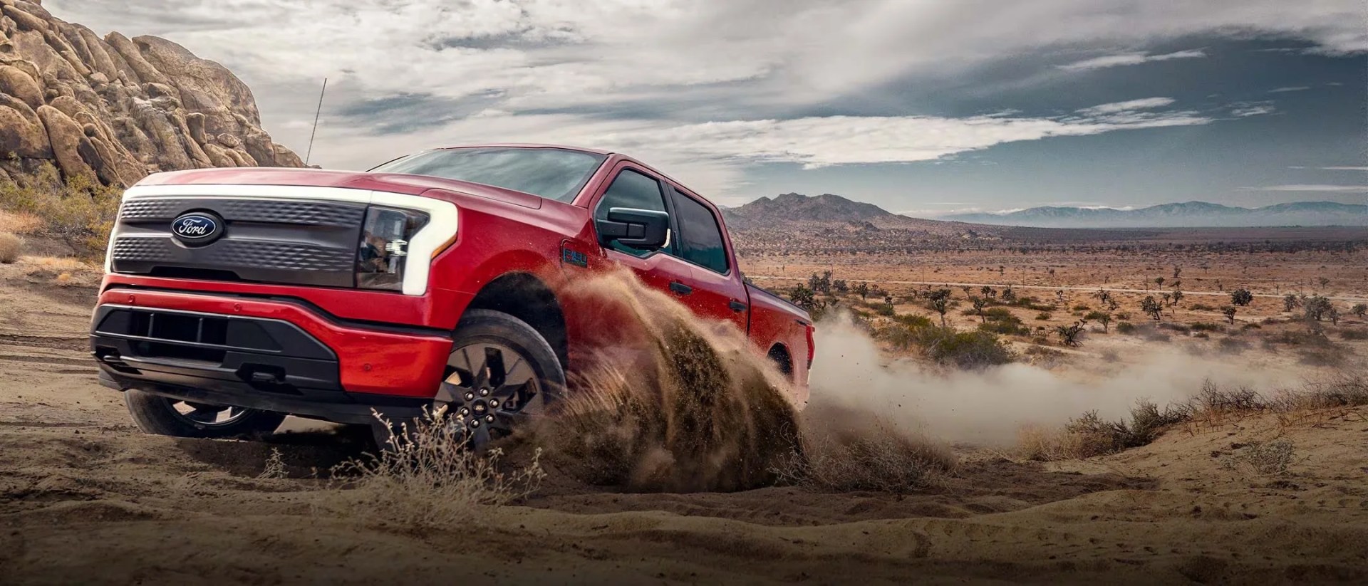 red ford electric pickup truck kicks up sand in the desert