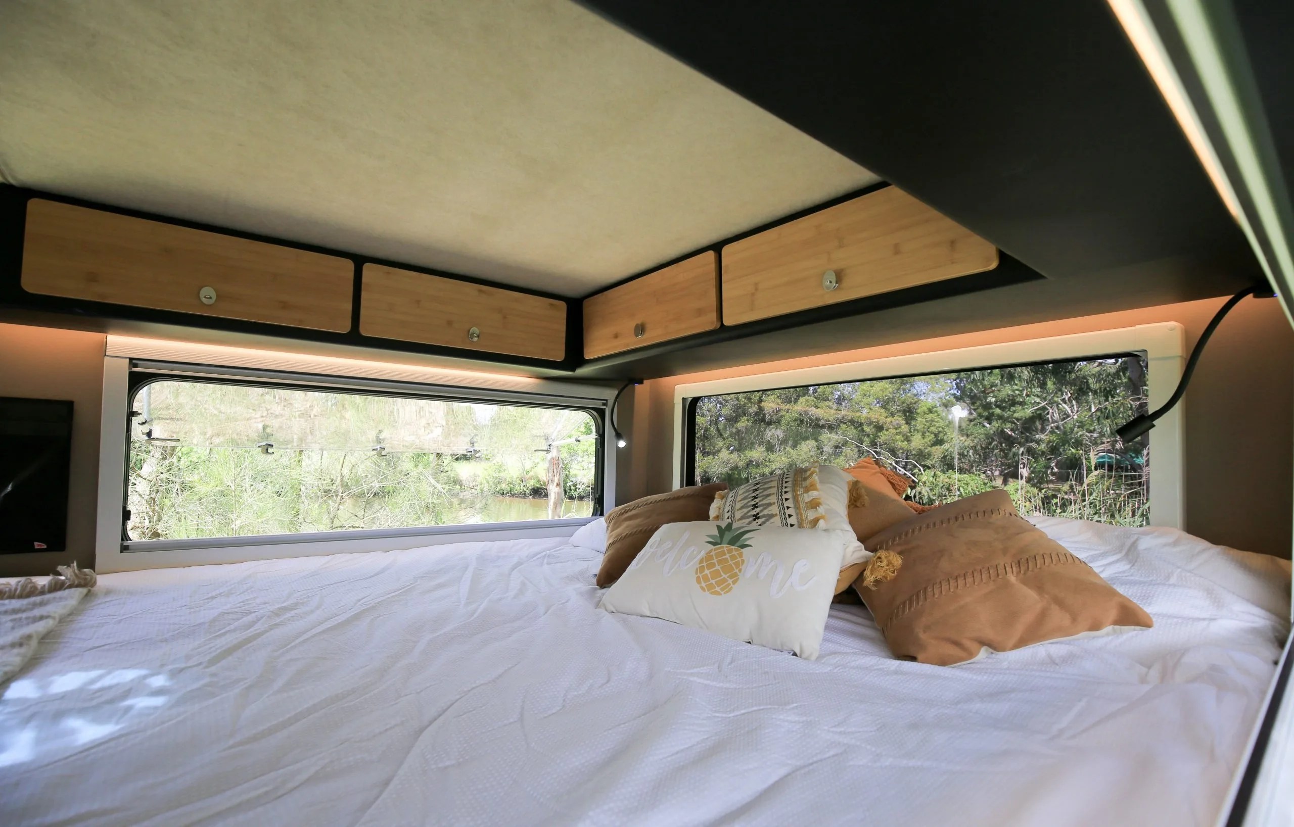 a bed surrounded by expansive windows inside a Kimberly Kampers camper