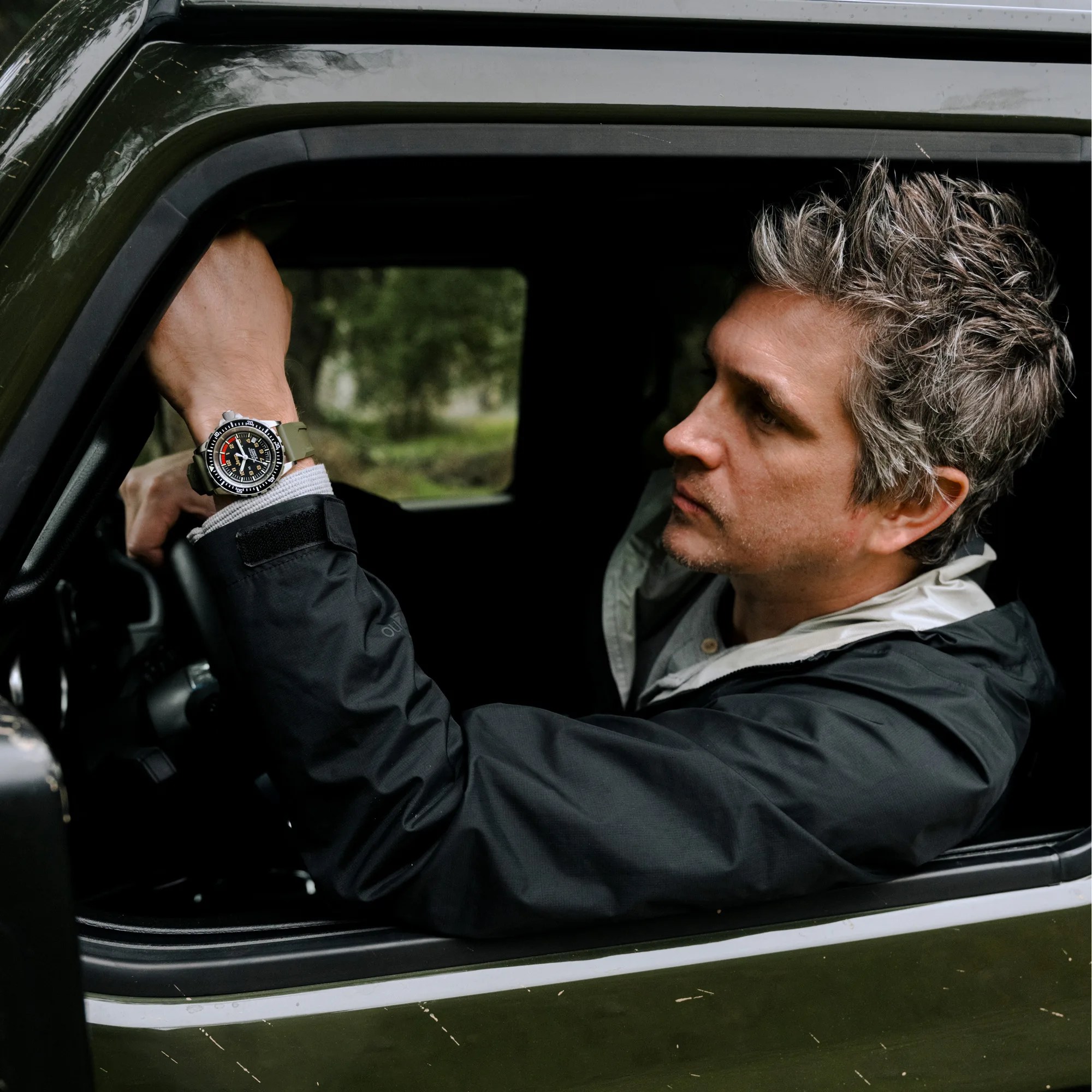 man drives a jeep wearing a marathon dive watch