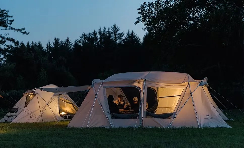 Two Snow Peak tents lit up by lanterns in the twilight with people inside.