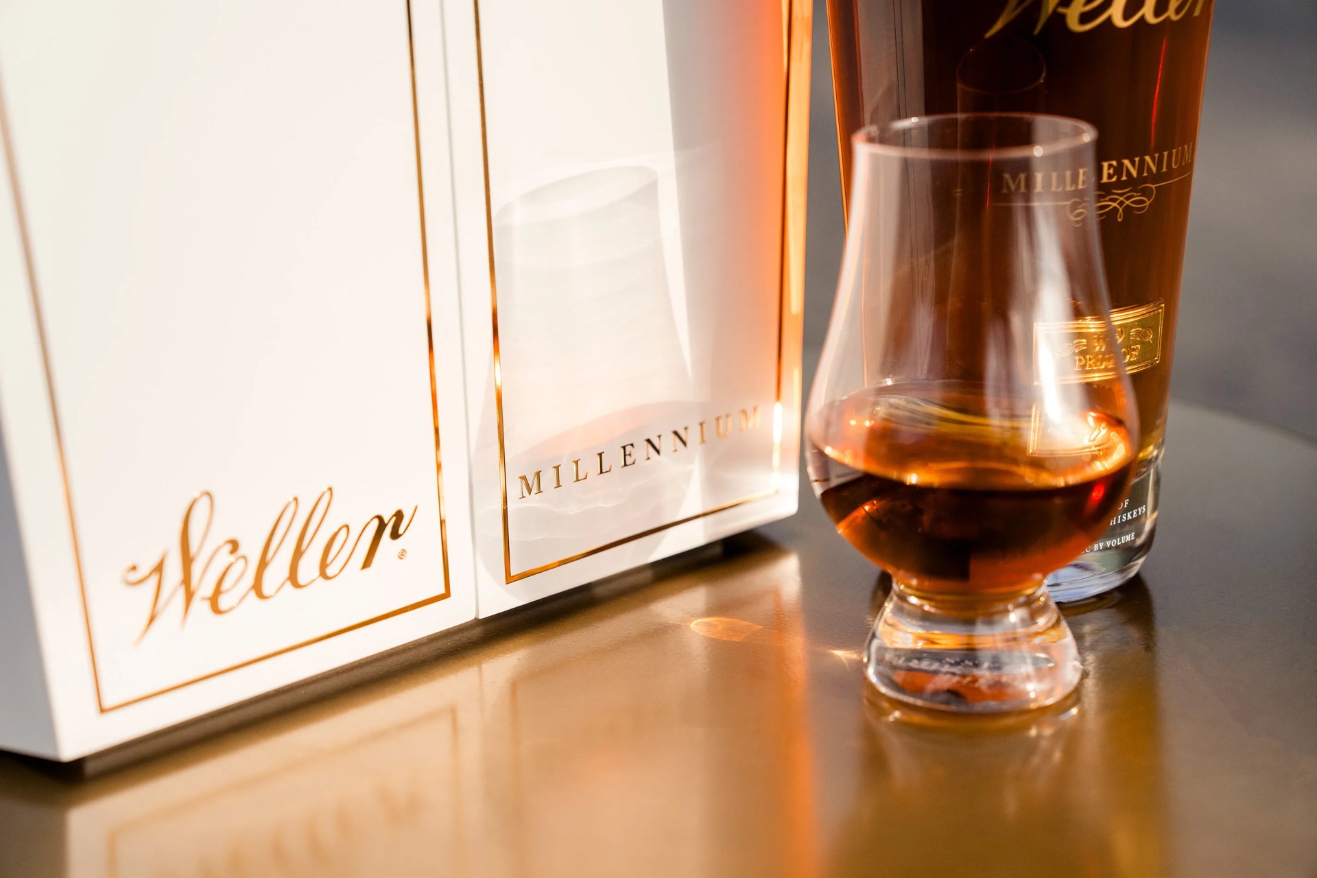 A glencarin of Weller Millennium sitting next to its white display case and in front of a full bottle. 
