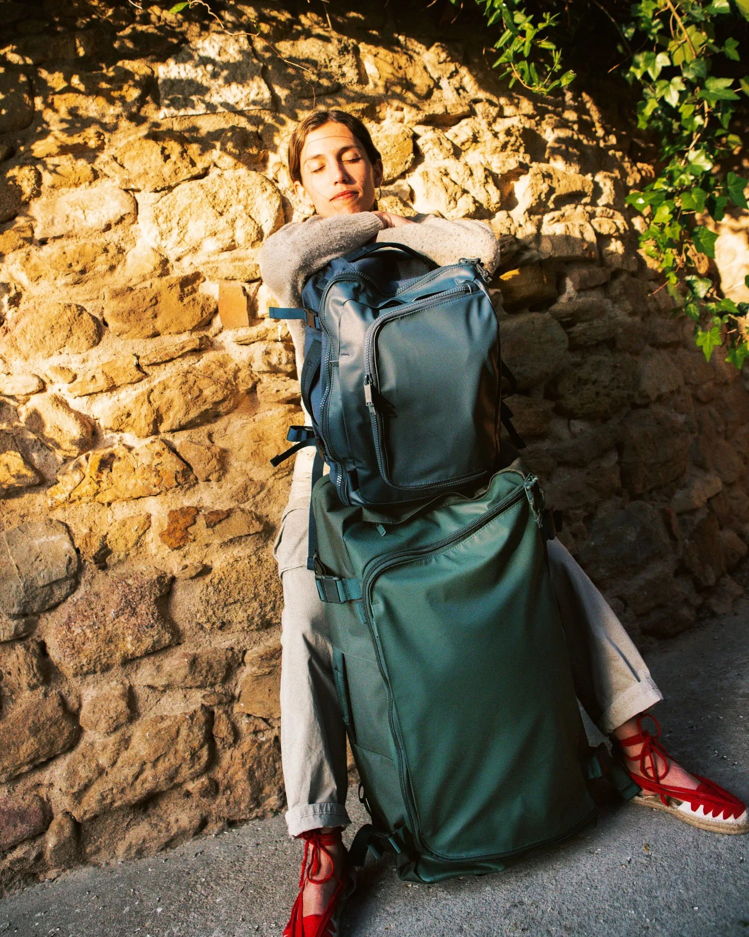 woman sitting with a backpack resting on top of a green suitcase