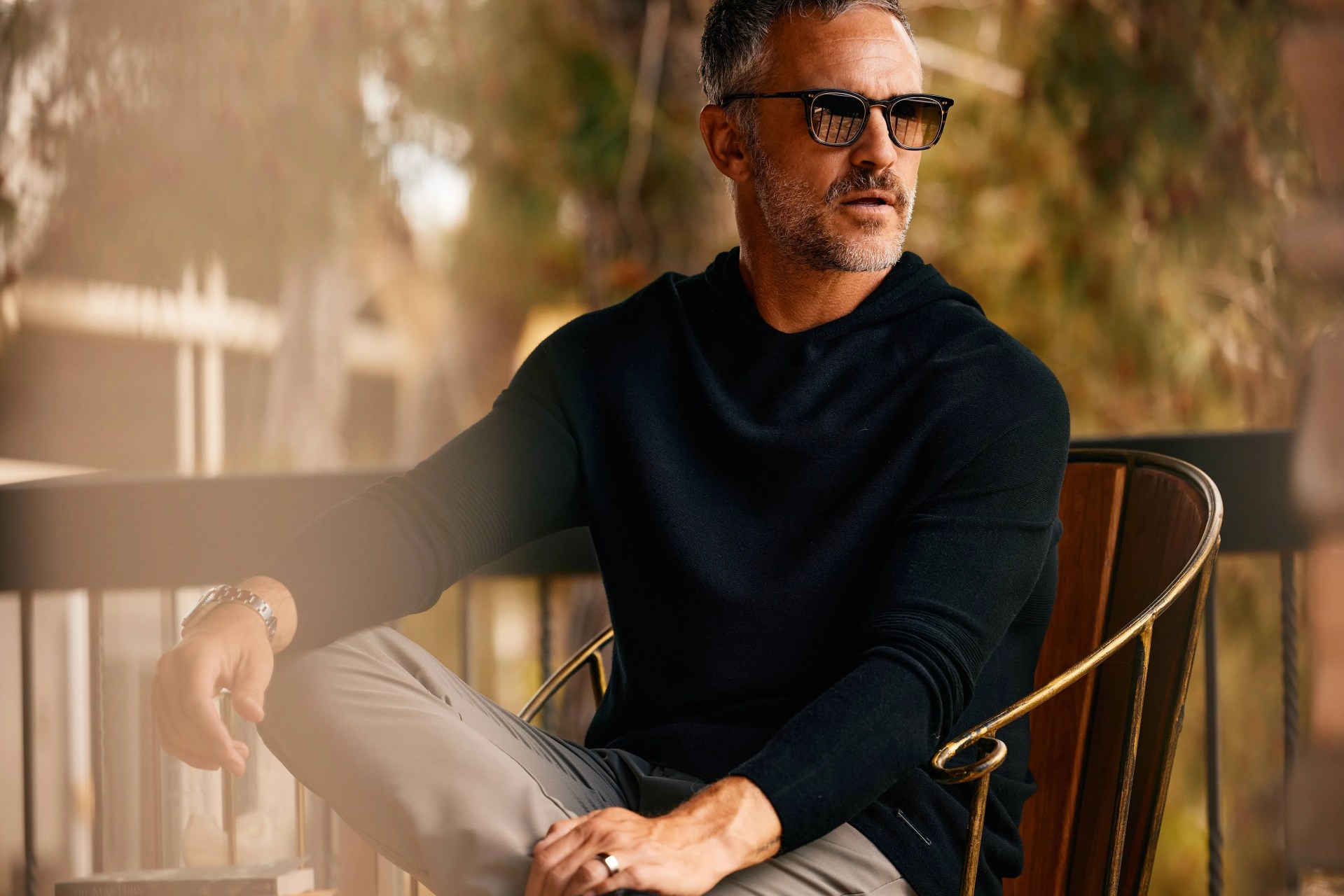 a man sits in a chair wearing sunglasses and a black hoodie