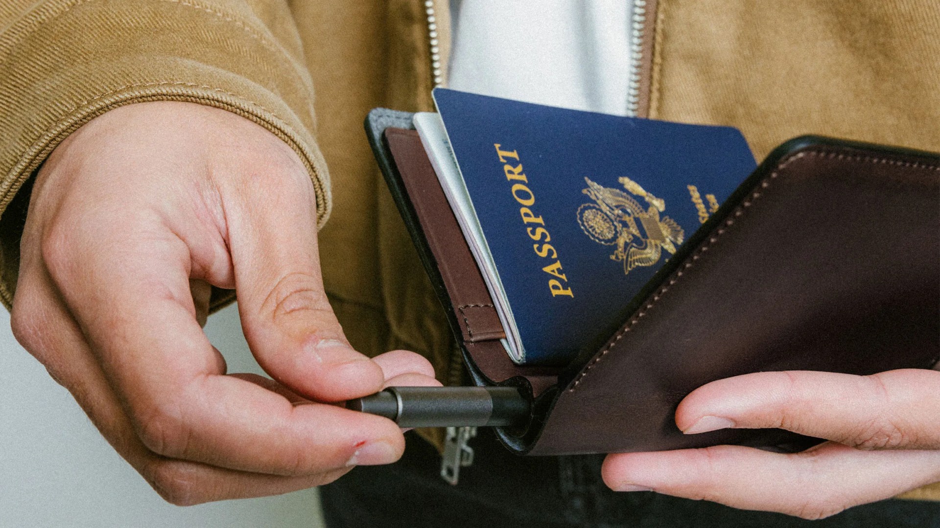 Nomad Passport wallet being held in one hand by model while the other hand is pulling out the integrated pen