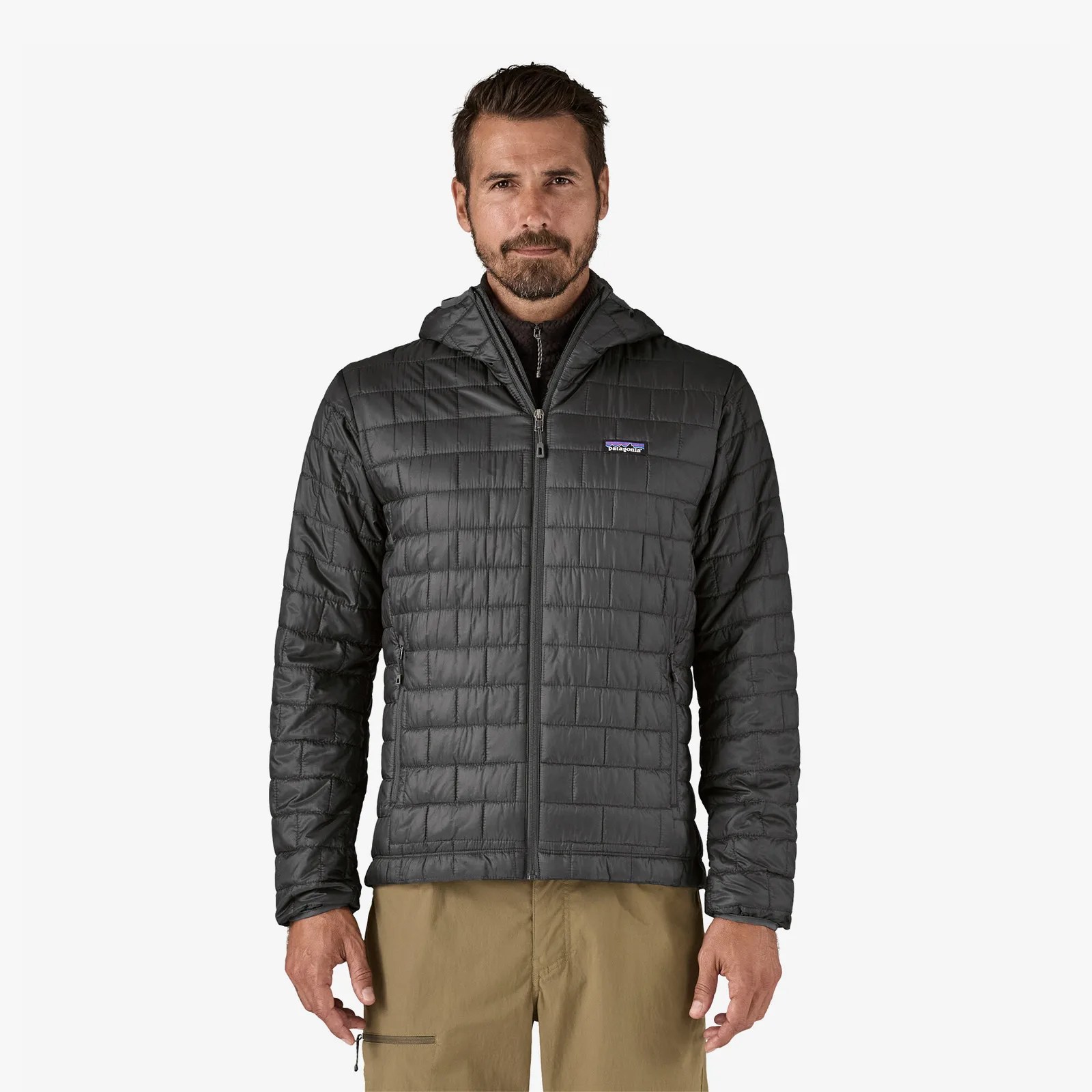 A white male with a beard wearing a dark grey colored Patagonia Nano Puff hooded jacket looking straight ahead. The model is shown from the waist up.