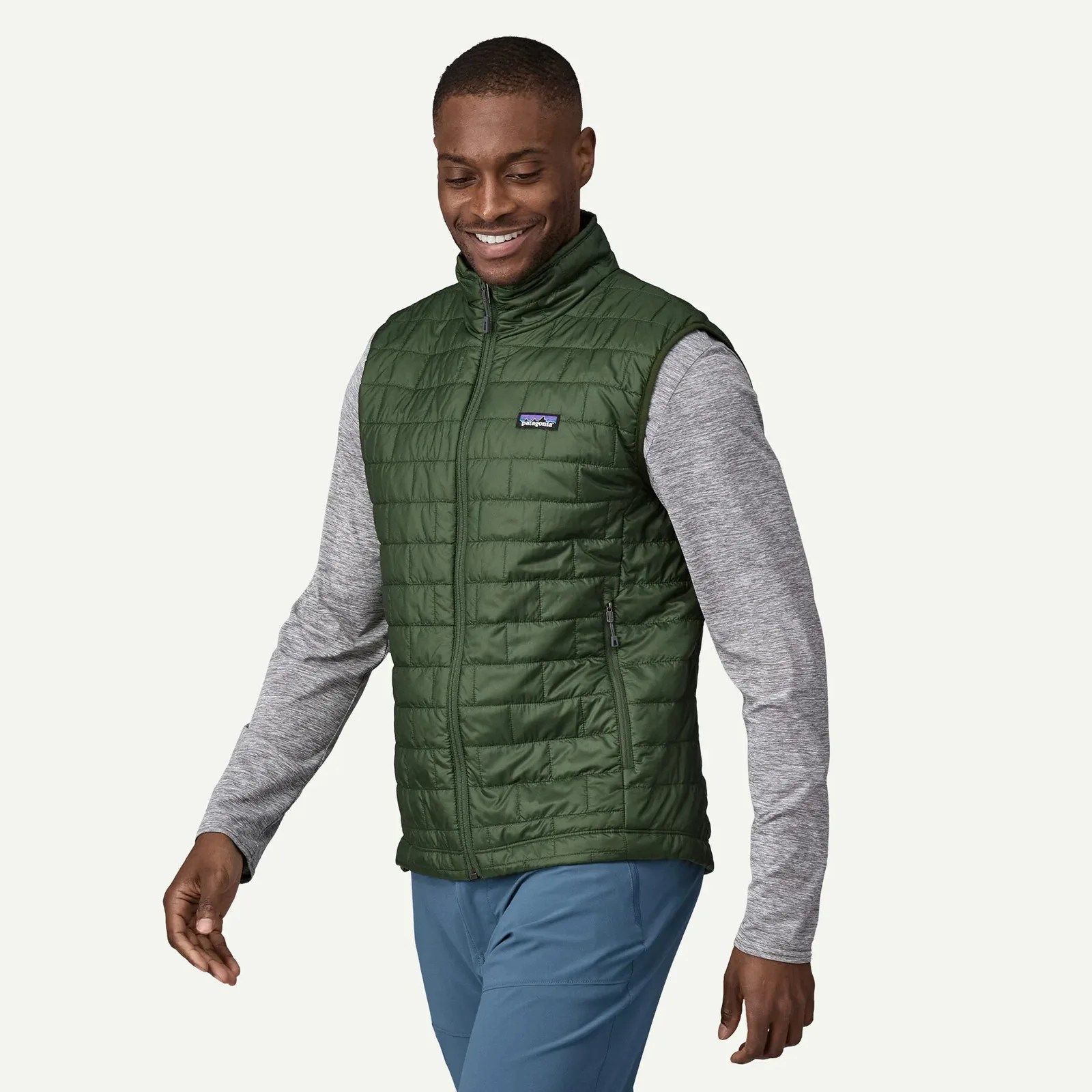 A black male model wearing a green Patagonia Nano vest shown from the knees up smiling and facing to the left