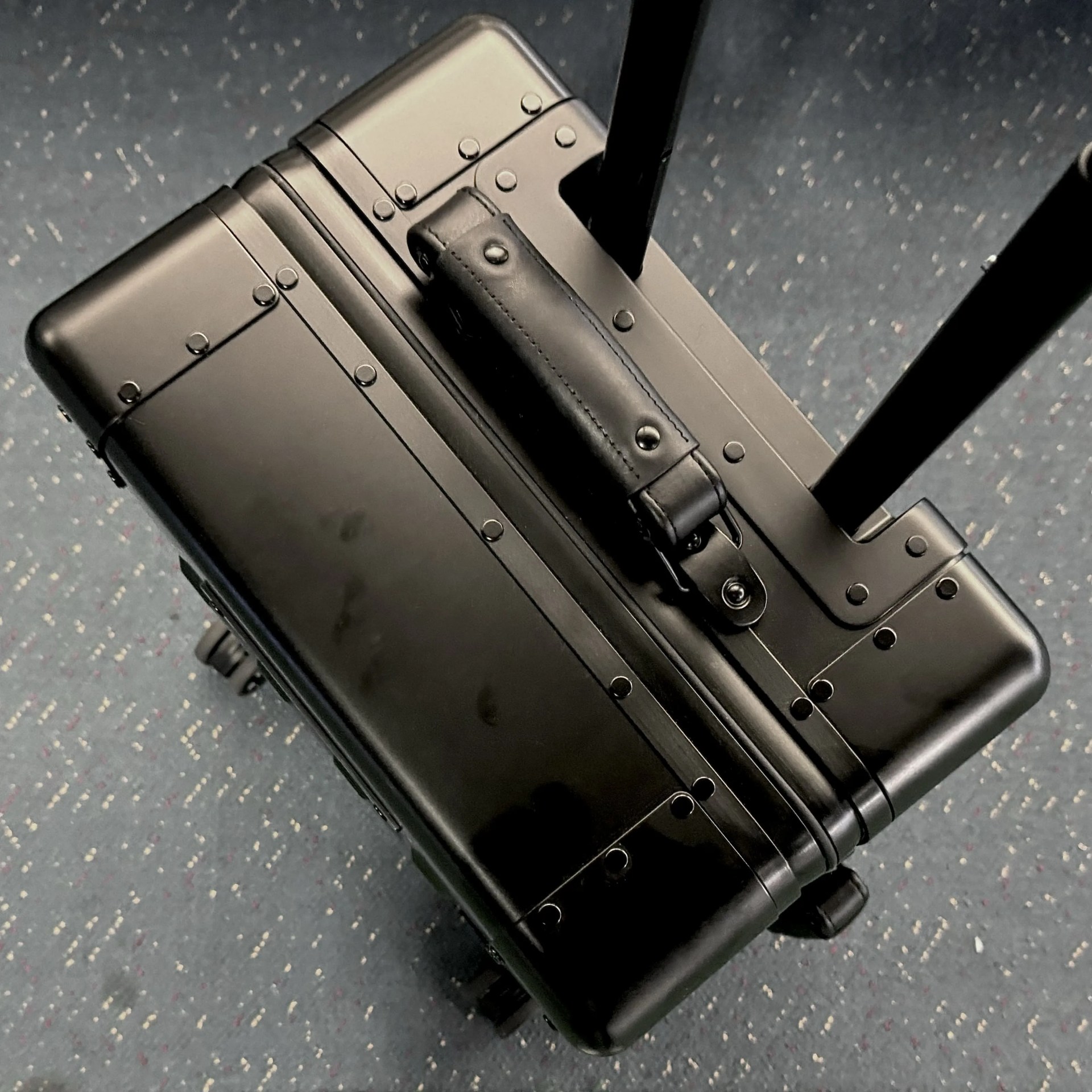 Top down image of Sterling Pacific’s Cabin Travel Case 40L aluminum hard sided luggage showing visible finger prints on the shiny black exterior.  