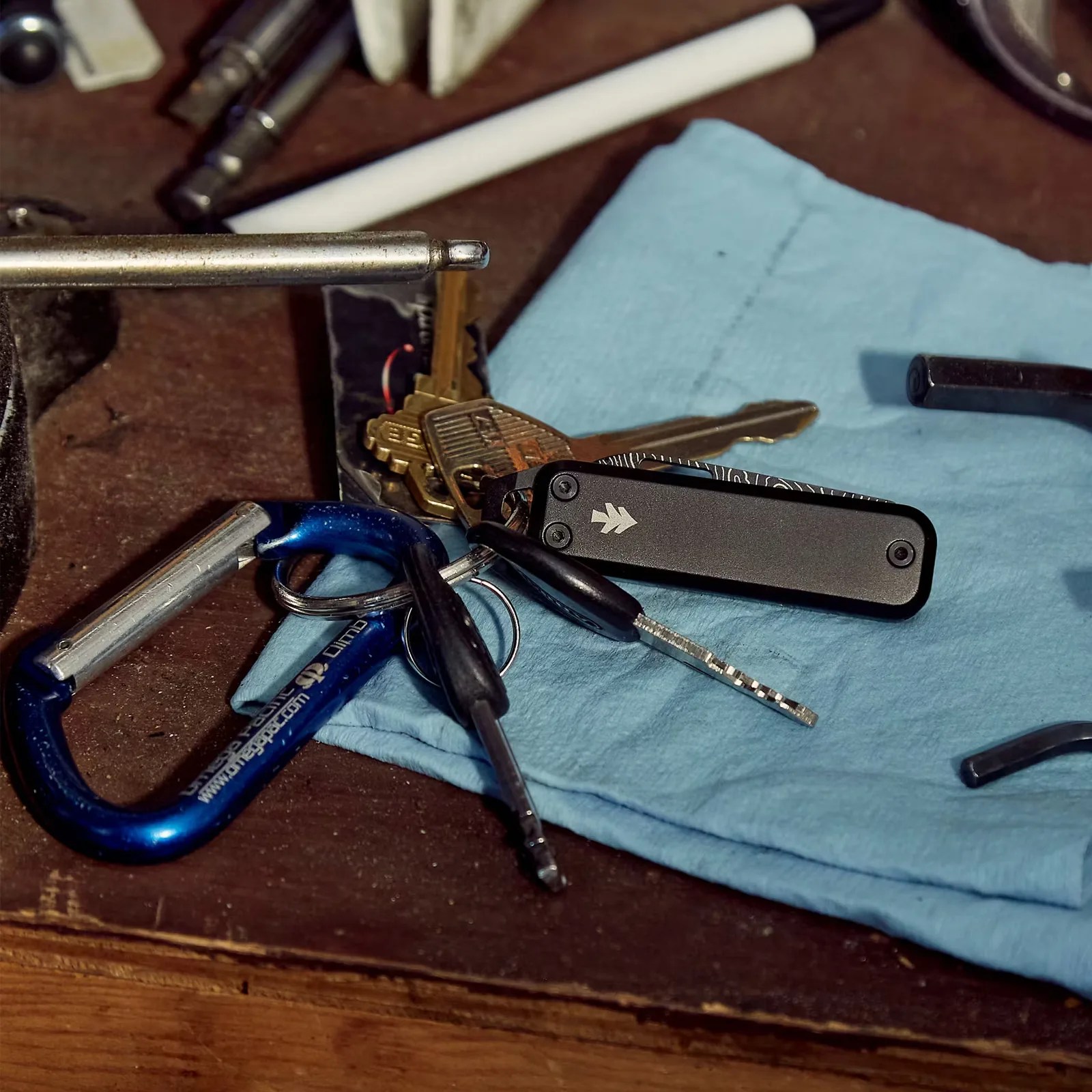 The James Brand Elko knife in black shown on a keyring resting on a wooden table.