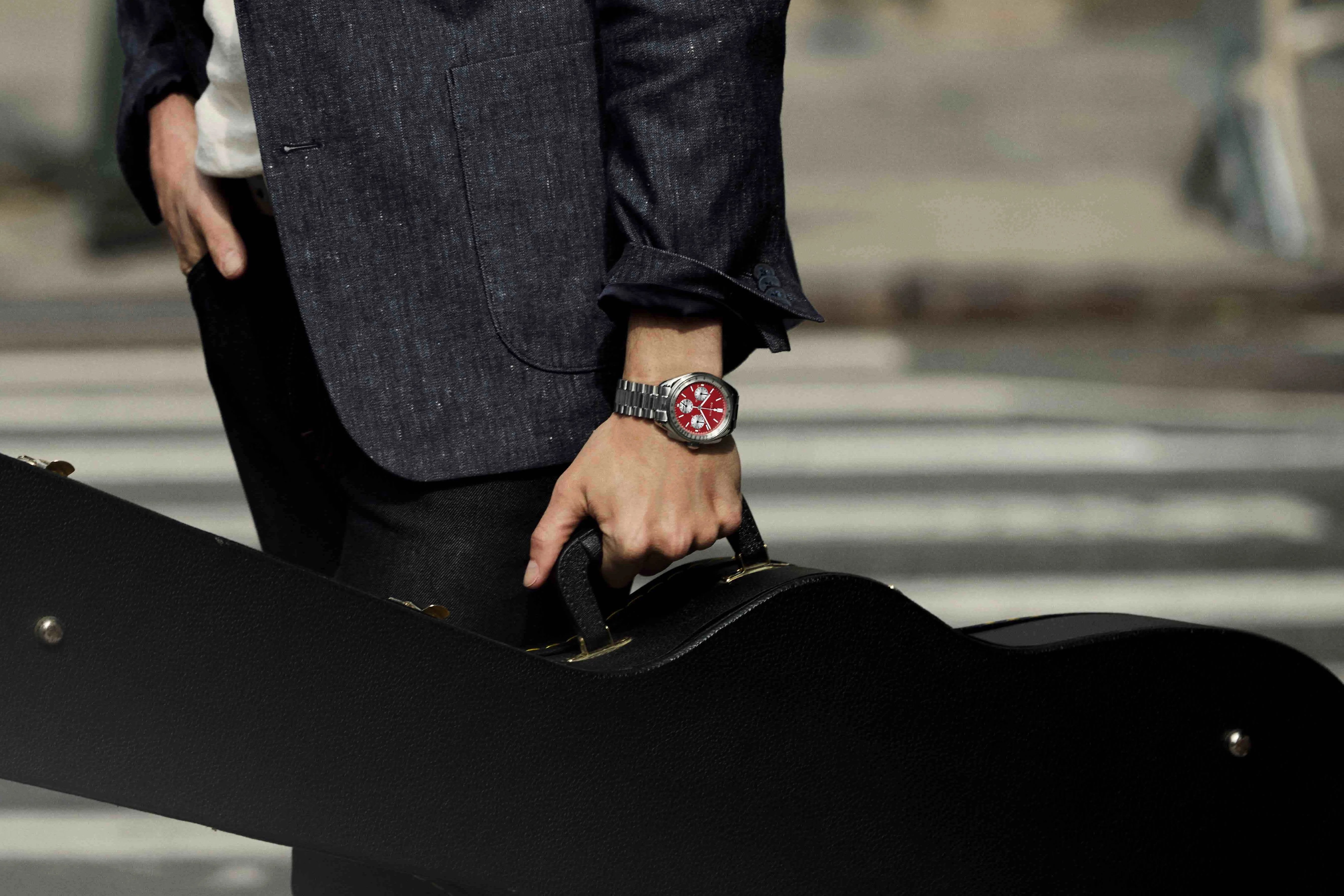 man carries a guitar across the street wearing a bulova watch