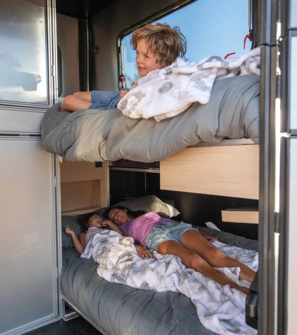a women and two children relax on bunk beds inside an exodus camper
