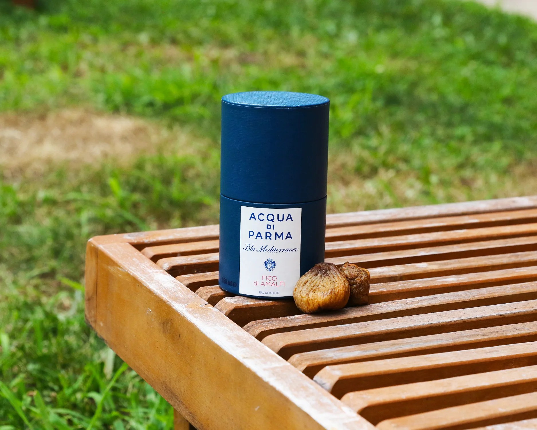 acqua di parma fragrance bottle on a slatted bench next to some dried figs