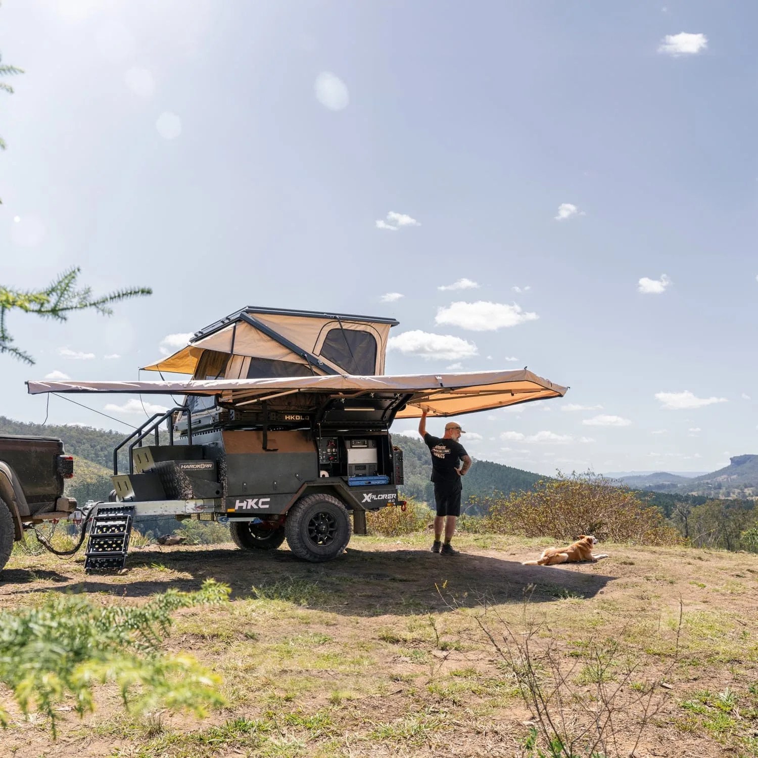 a man and a dog next to a hardkore campers trailer in the wilderness