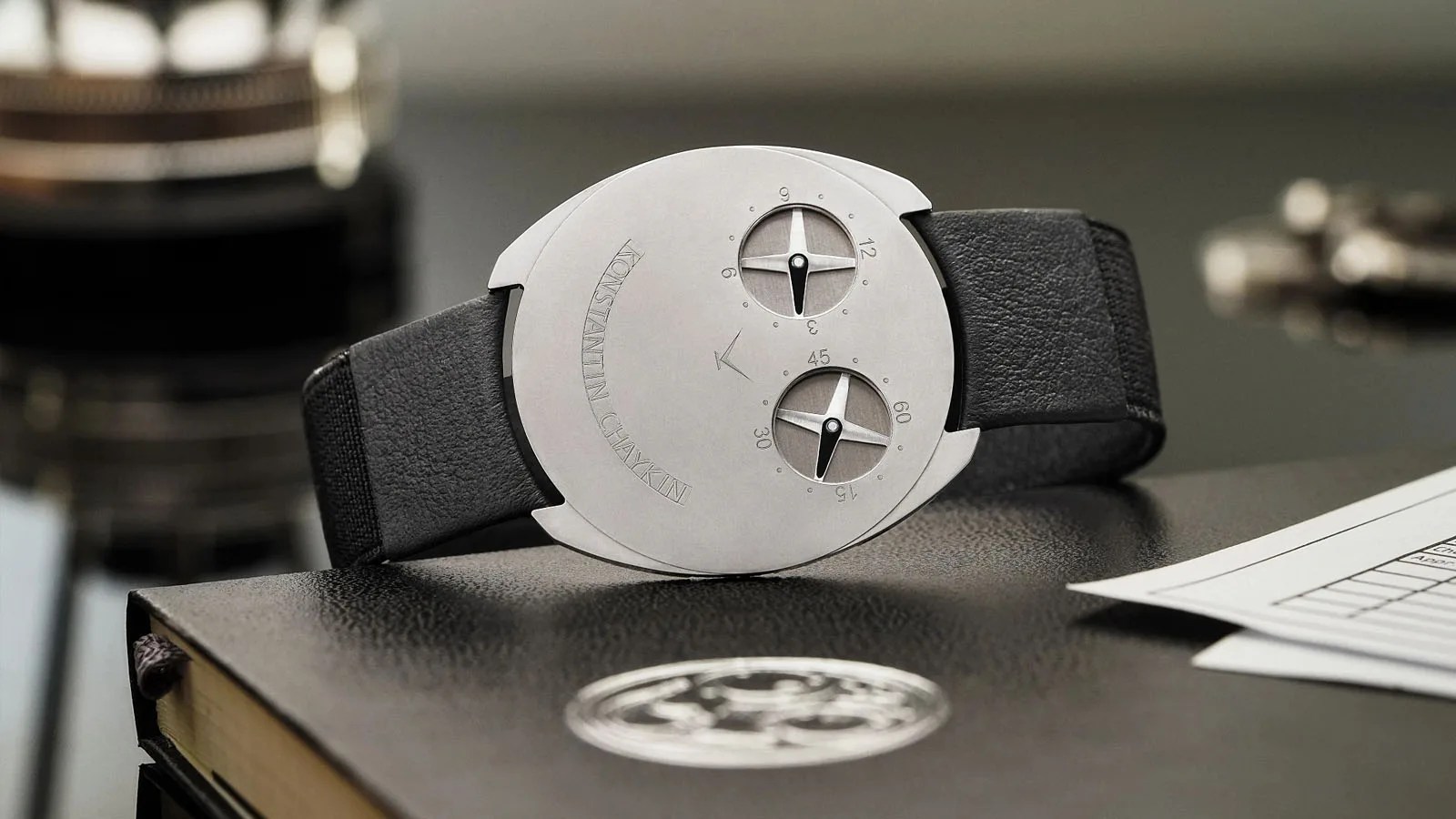 Konstatin Chaykin ThinKing watch sitting on a table on its side behind a piece of an ultra-thin watch movement