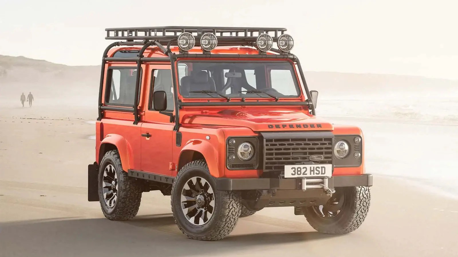 A Land Rover Classic Defender V8 in red parked on a beach.