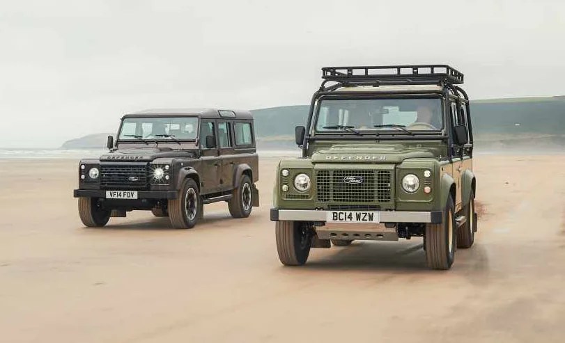 Two restored classic Land Rover Defenders parked on a beach.
