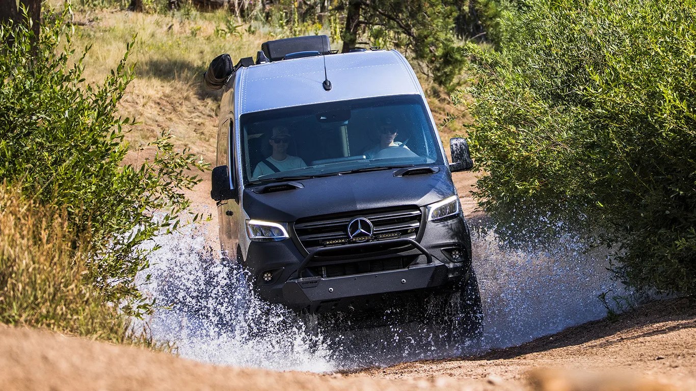 an airstream camper van drives through a puddle