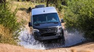 an airstream camper van drives through a puddle