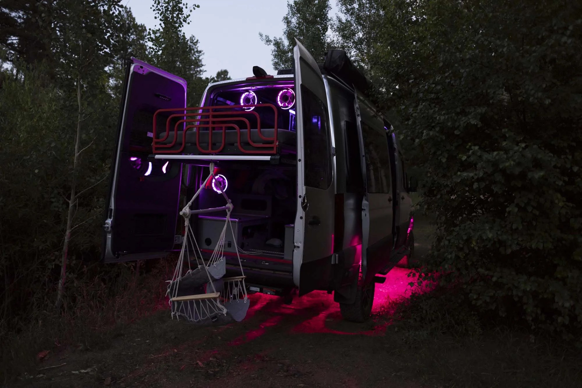 an airstream camper van with lots of mutlicolored lights parked in the woods