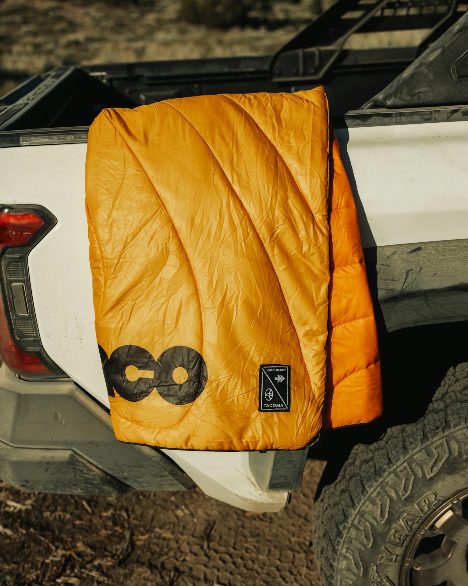 a tacoma branded rumpl blanket from huckberry is slung over the bed of a toyota tacoma pickup truck