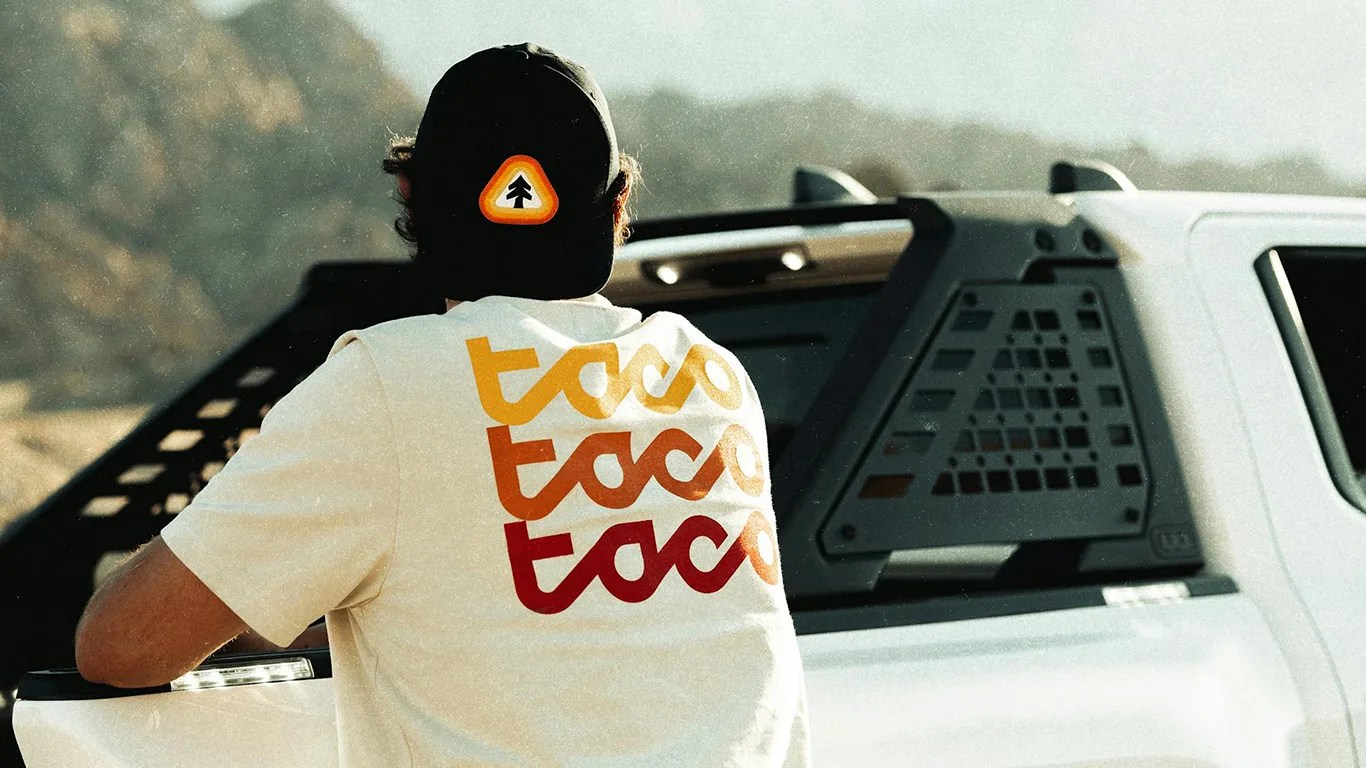 a man wears huckberry clothing while leaning on a toyota tacoma truck