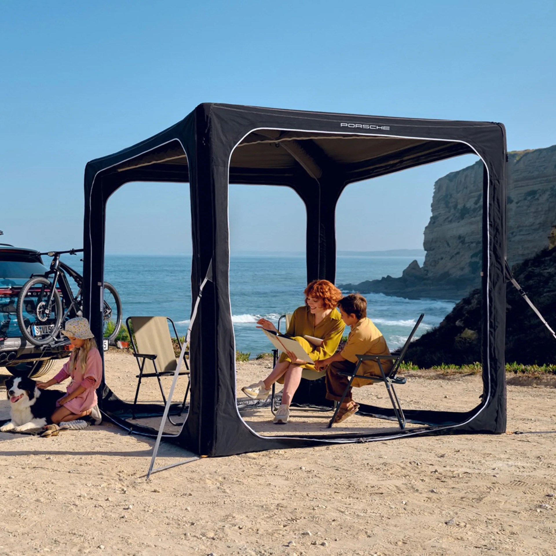 a family sits on chairs inside a large porsche tent on a beach