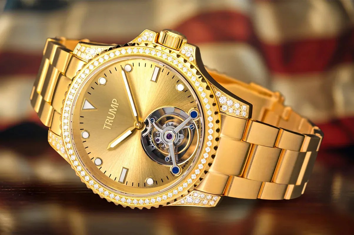 Trump Watches Victory Tourbillion in gold shown at angle with a blurred American flag in background. 