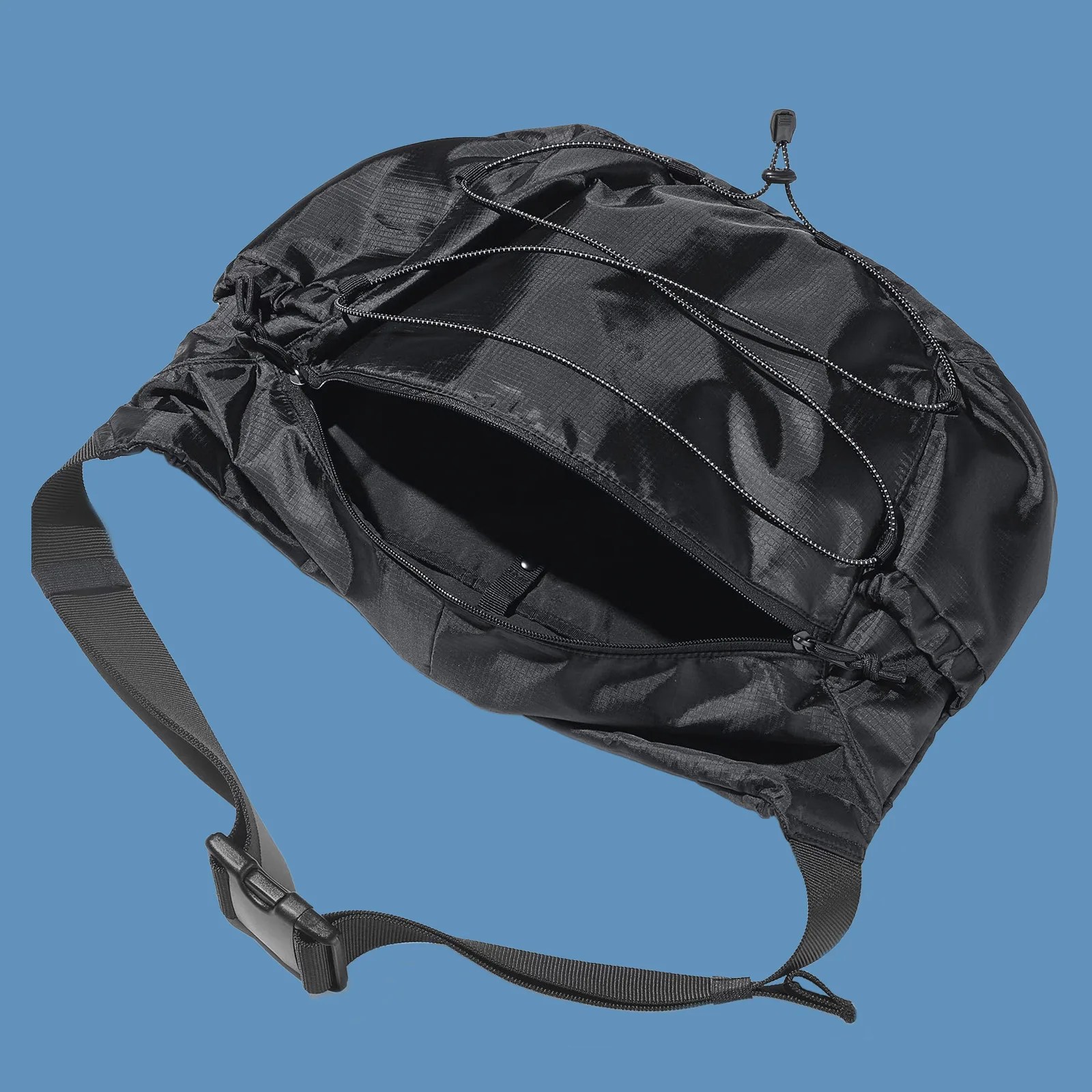 Gu Ripstop messenger bag in black shown empty and laid flat with main compartment open to reveal its interior pockets against a solid blue background