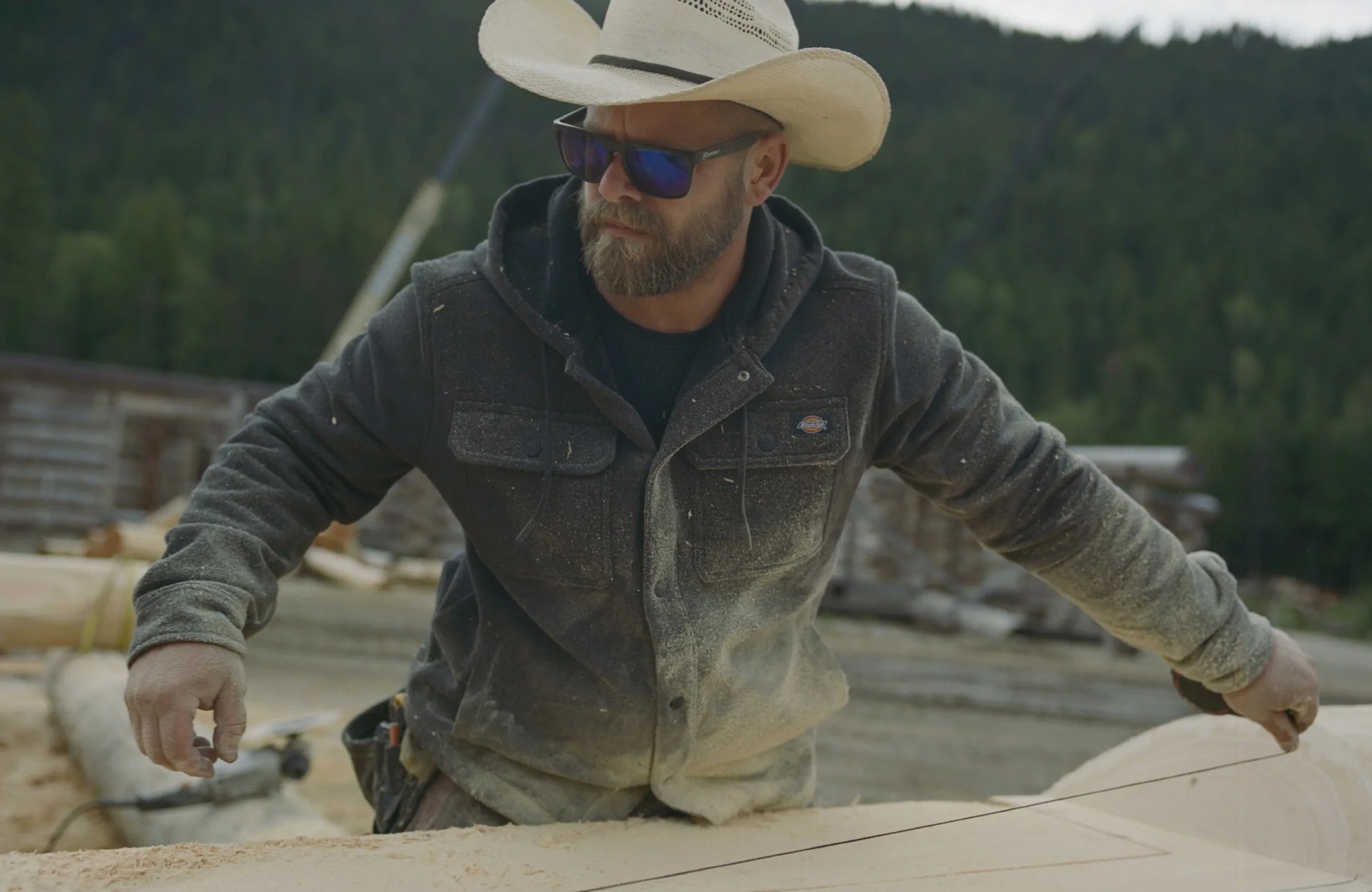 A man in a cowboy measures a line on a large timber log