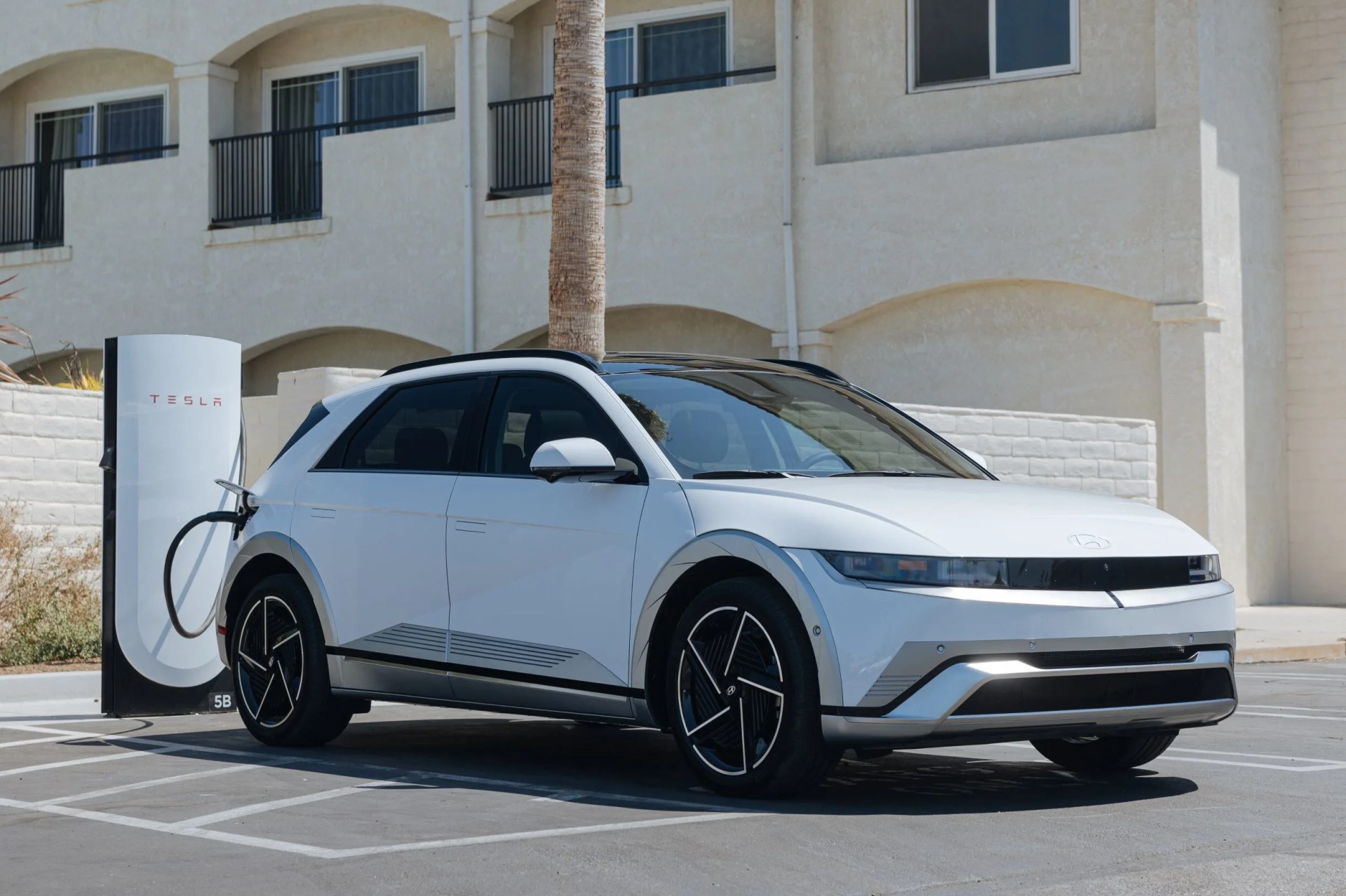 A white 2025 Hyundai Ioniq 5 parked and charging at a Tesla Supercharging station.