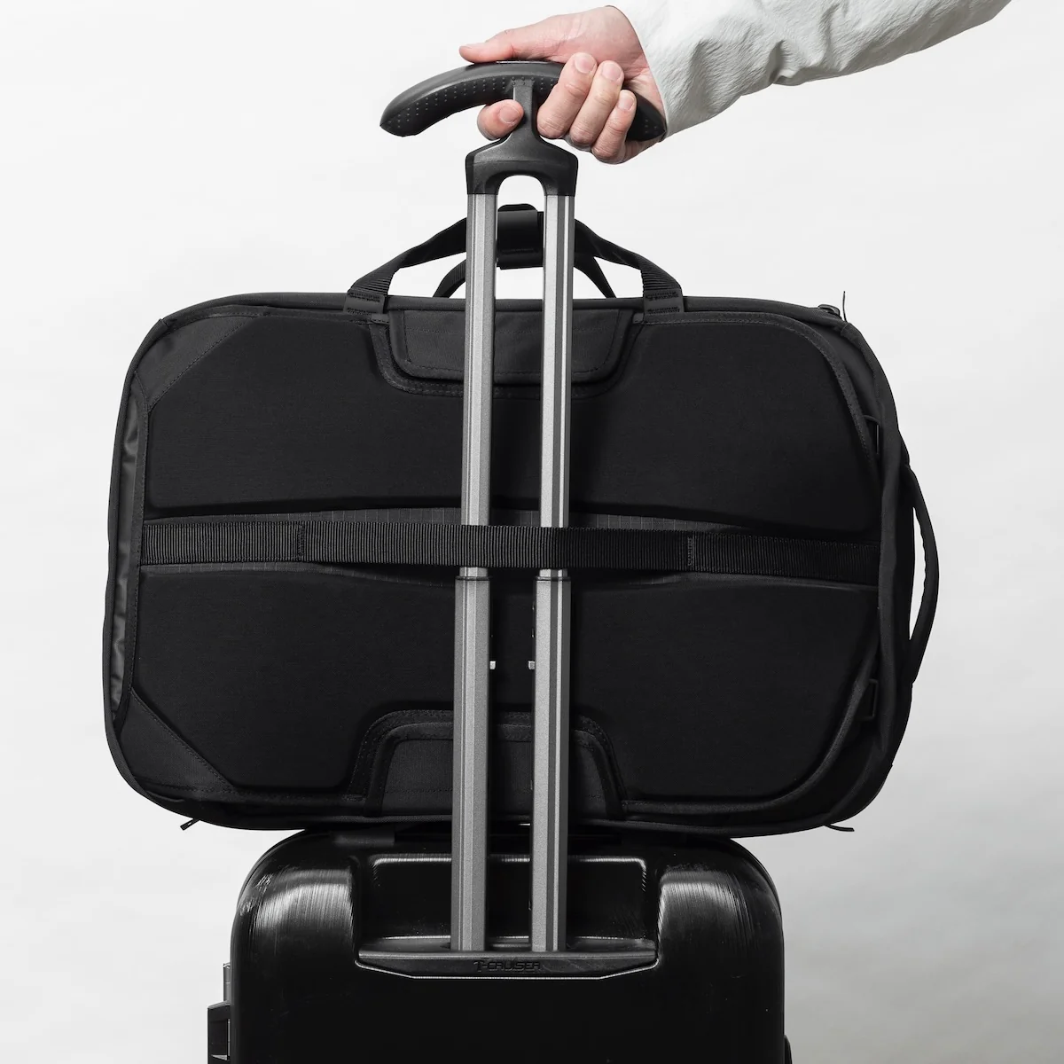 The Black Ember Forge 40 Travel backpack shown attached to a rollaboard suit handle. 