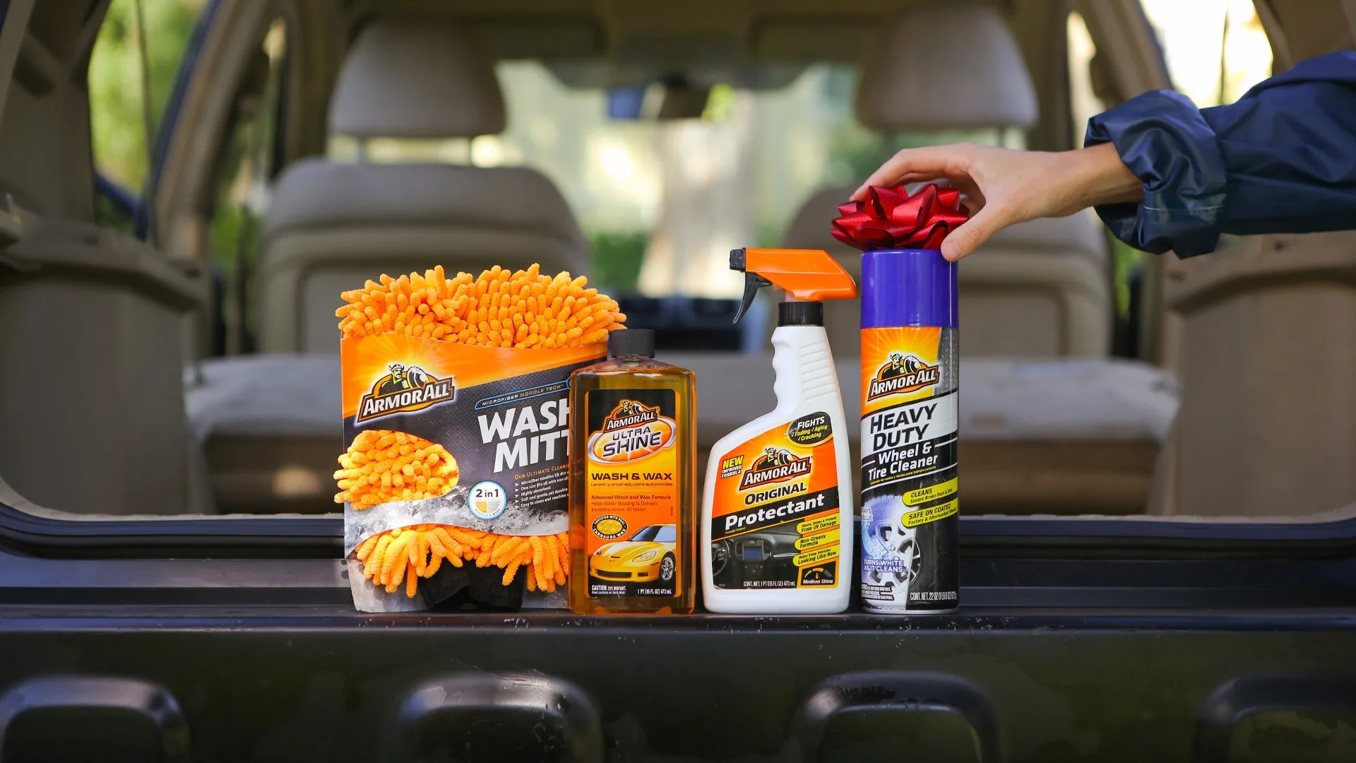 Armor All cleaning supplies in a trunk with a hand placing a bow tie on one product
