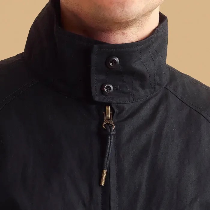 A close up of the buttoned up neck cuff of the Billy Reid Hunting Jacket being worn by a male model. The models chin is barely visible. The image background is a light tan color. 