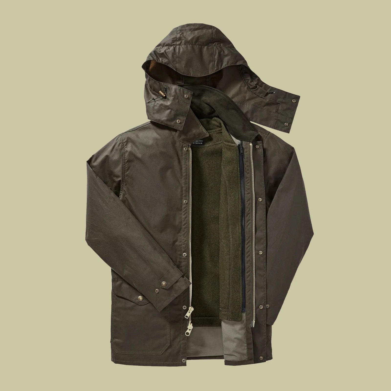 Filson Cover Cloth Mile Marker Coat shown laid flat and open to reveal how an extra liner can zip into the jacket for warm. Shown on a taupe background.