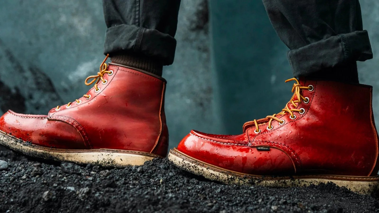 A close up ankle shot of someone wearing a pair of Red Wing Heritage Gore-Tex Moc Boot Books walking on black pebbles wearing navy pants