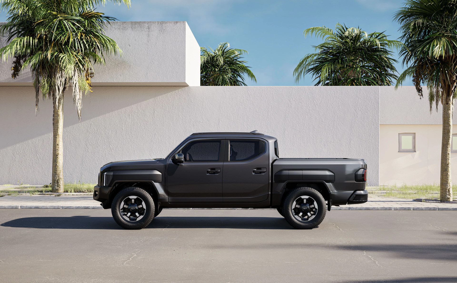 An image of the Kia Tasman parked on a sunny street flanked by palm trees. The dark grey colored truck is shown in a profile few facing left to right.