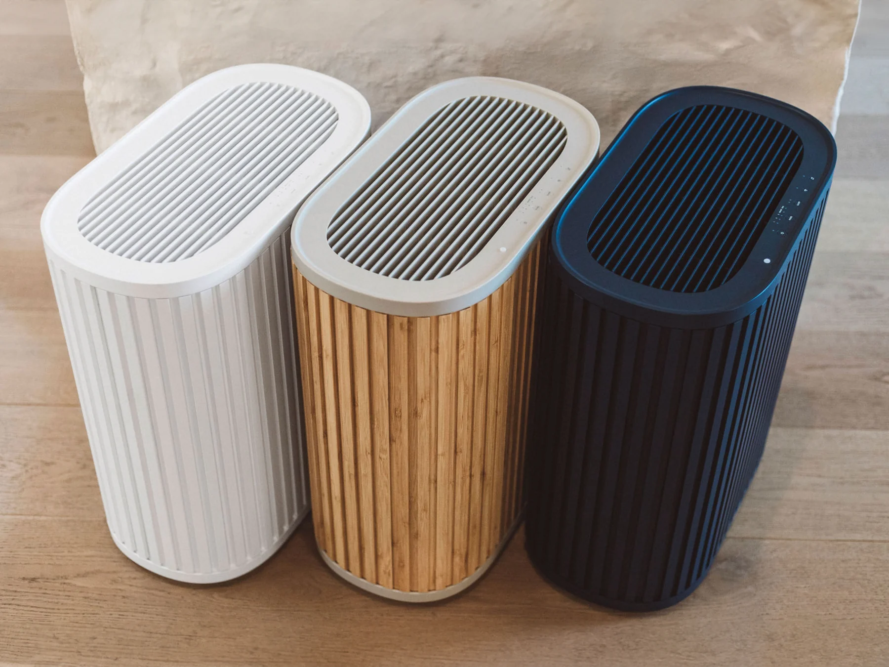 Three Windmill Air Purifiers sitting side-by-side at an angle One is white, one is natural bamboo colored and the other is navy. 