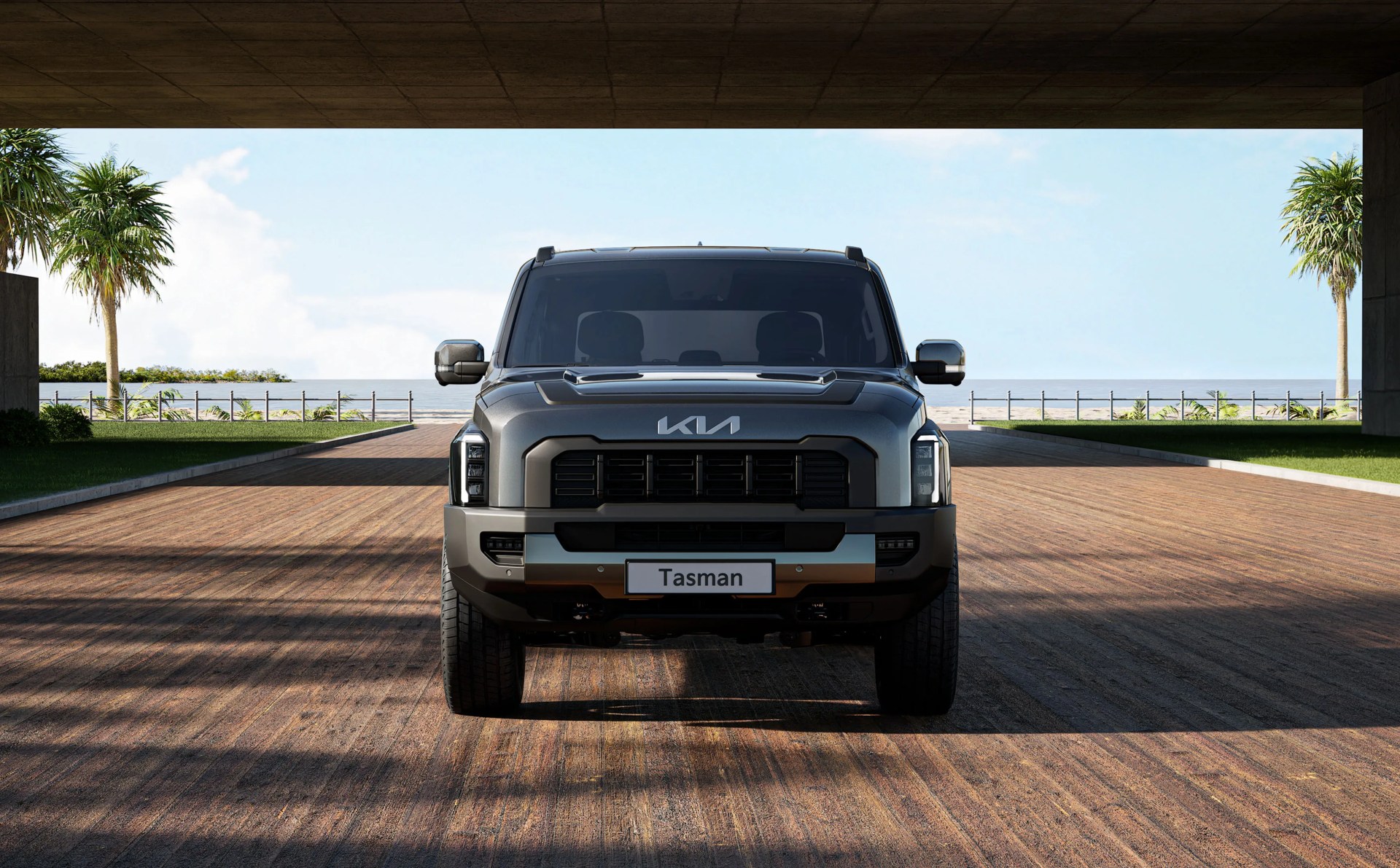 A rendering o the Kia Tasman truck shown head up to highlight the grill detailing. The truck is blackish / grey and parked on what appears to be a large wooden piece with a beach and the ocean as a backdrop.