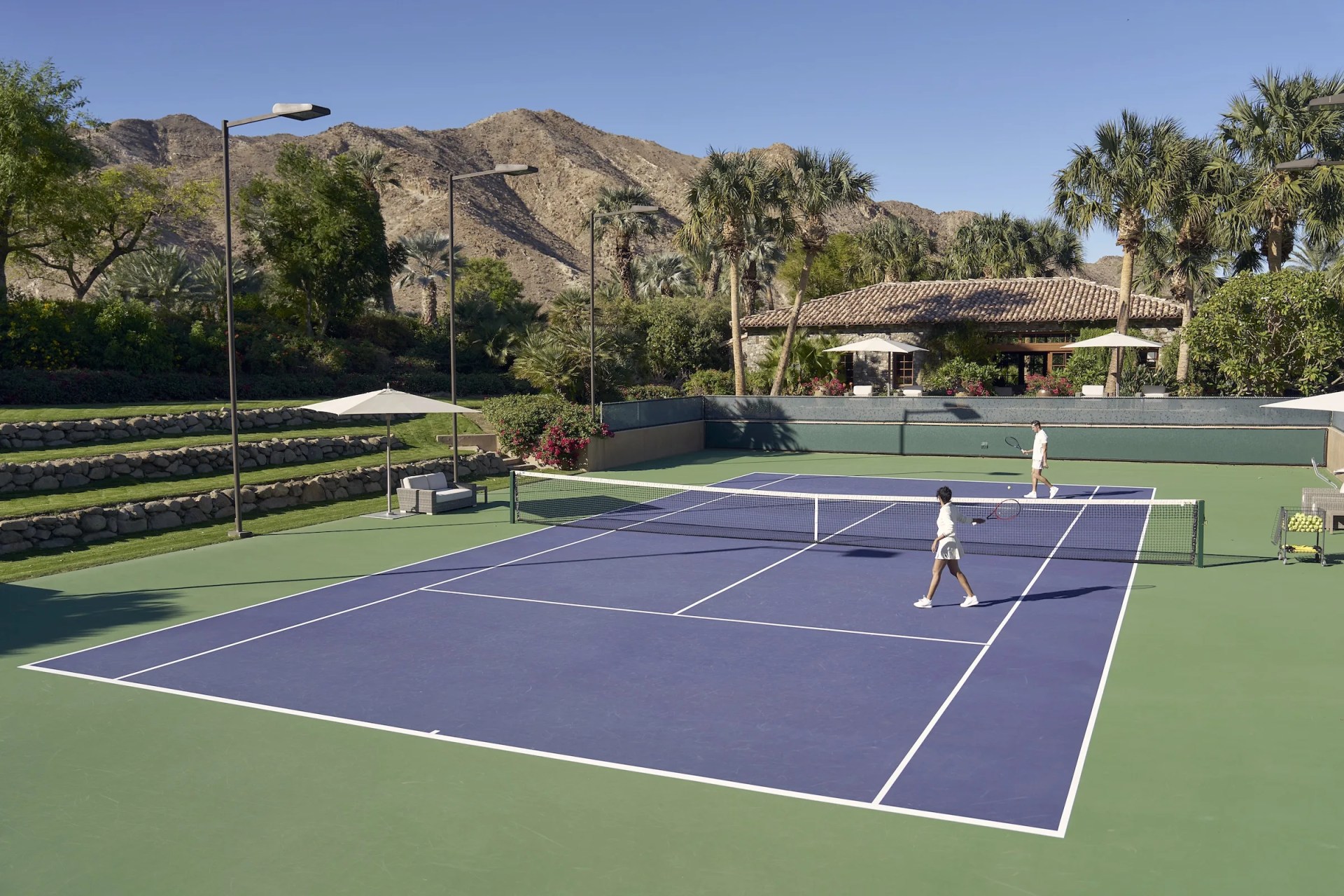 Two people walk onto a blue tennis court