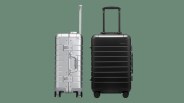 Two away aluminum suitcases sitting next to each other against a dark green background. The left bag is silver and shown in profile. The right black is metallic black and shown head on.