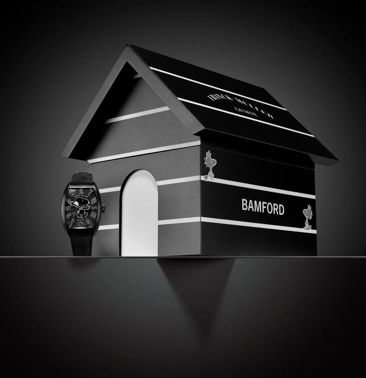 The Frank Muller Crazy Love Snoopy Watch positioned next to a black and white 3D modeled version of Snoopy's iconic Dog House. The house is facing at an angle with the door to the dog house angled to the left side of the image. The Frank Muller wordmark is on the dog house roof. The Bamford wordmark is on the side of the hoouse.