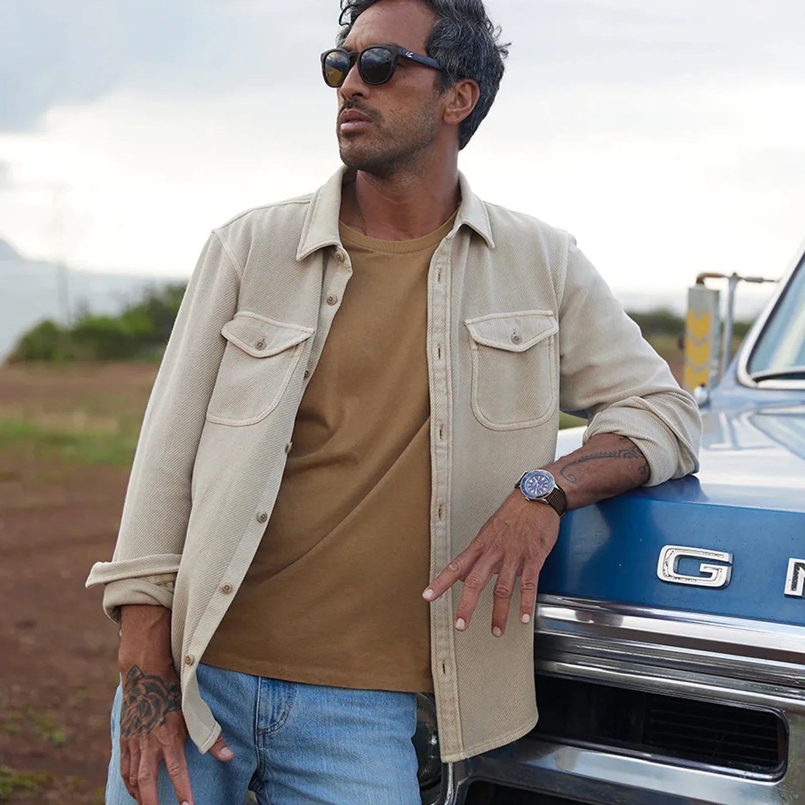 Man leaning on trunk wearing Outerknown's Chroma blanket shirt in a light yellow color.