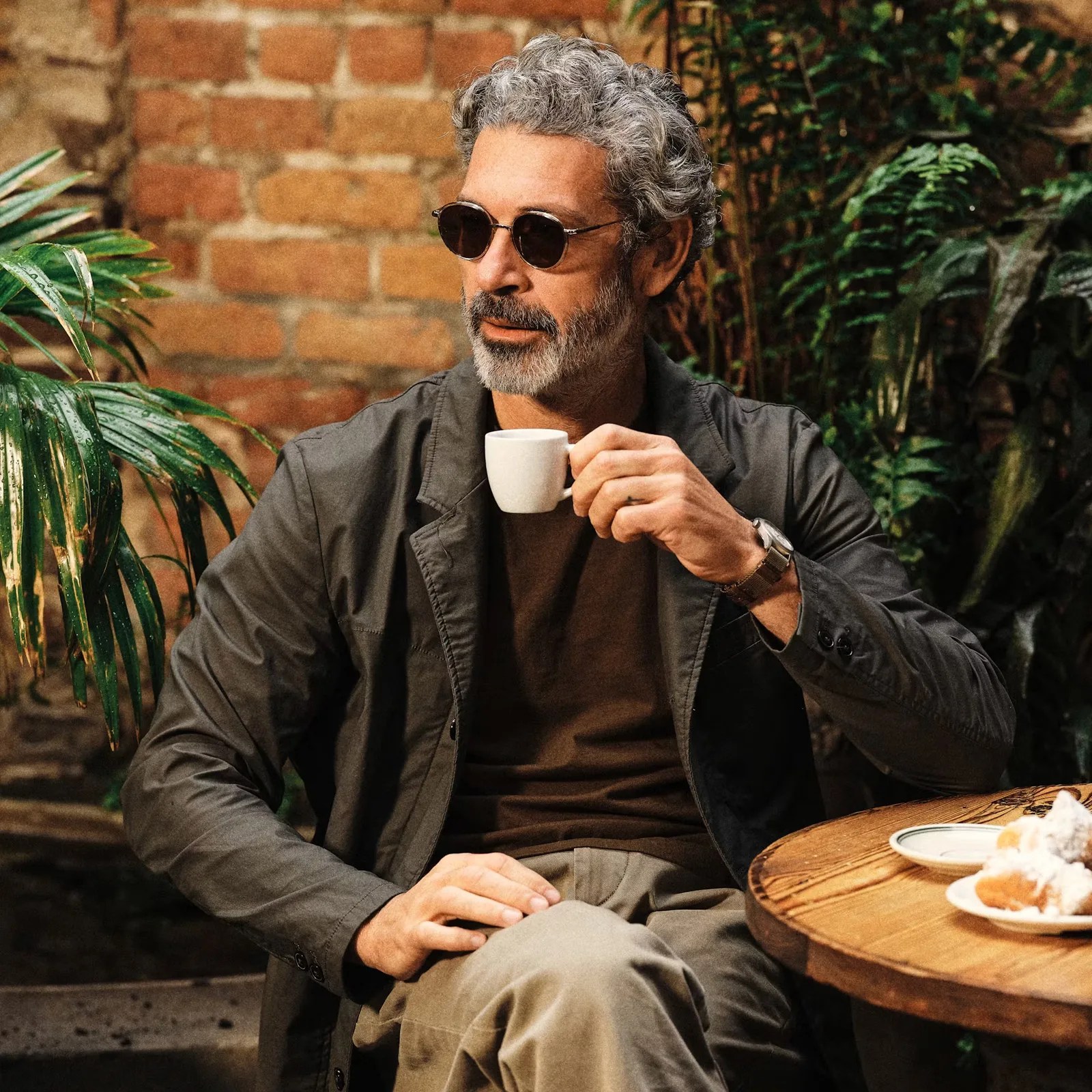 A man wearing the Relwan Flex Blazer in Grey sitting at table drinking an esspresso